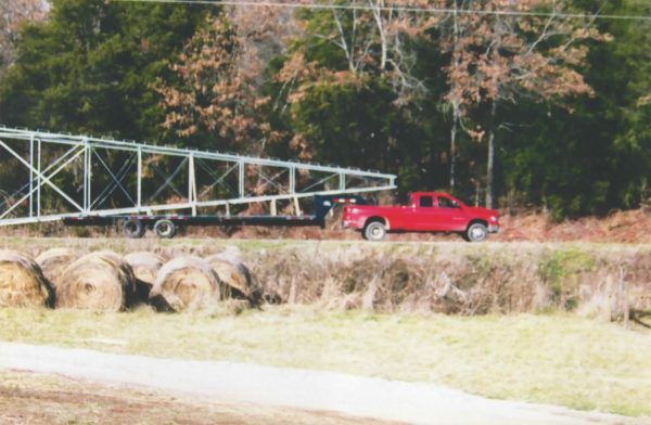 A red truck is driving through a field with hay bales.