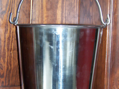 A metal bucket sitting on a wooden shelf.